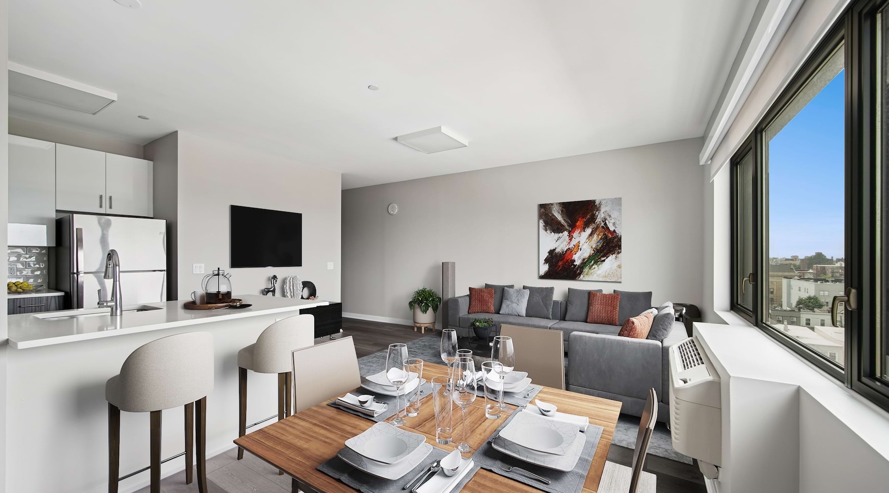 A living room and dining area with a couch, a table and chairs, and a kitchen with stainless steel appliances at The Station apartments in West New York, NJ.